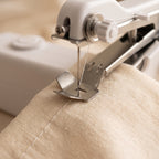 Close-up of the handheld sewing machine needle and presser foot stitching cotton fabric